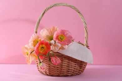 Photo of Beautiful poppy flowers in wicker basket on pink background, closeup