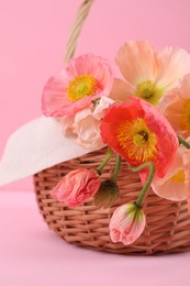 Photo of Beautiful poppy flowers in wicker basket on pink background, closeup