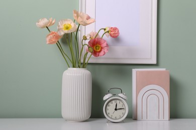 Photo of Beautiful poppy flowers in vase and decor on light table near green wall, closeup