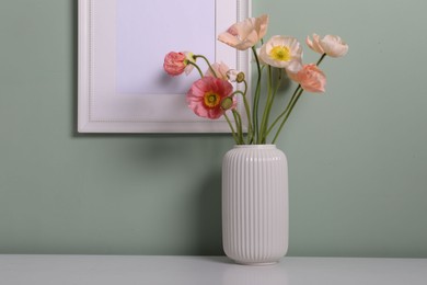 Photo of Beautiful poppy flowers in vase on light table near green wall, closeup