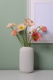 Photo of Beautiful poppy flowers in vase on light table near green wall, closeup