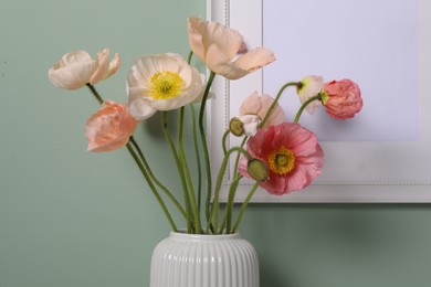 Photo of Beautiful poppy flowers in vase near green wall, closeup
