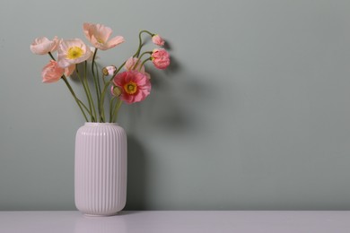 Photo of Beautiful poppy flowers in vase on light table against grey background, closeup. Space for text