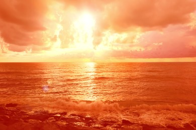 Image of Orange sky with clouds above sea during hot summer weather
