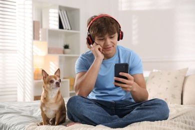 Photo of Teenage boy in headphones using smartphone and dog on bed at home