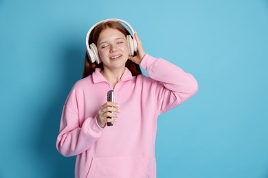 Photo of Smiling teenage girl in headphones with smartphone on light blue background
