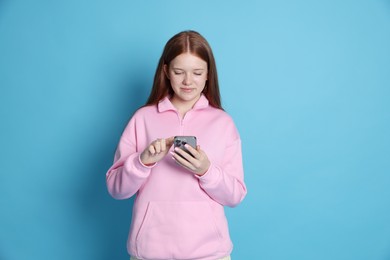 Photo of Beautiful teenage girl using smartphone on light blue background