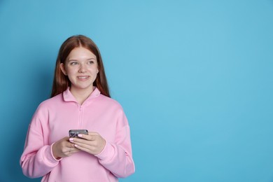 Photo of Smiling teenage girl with smartphone on light blue background. Space for text