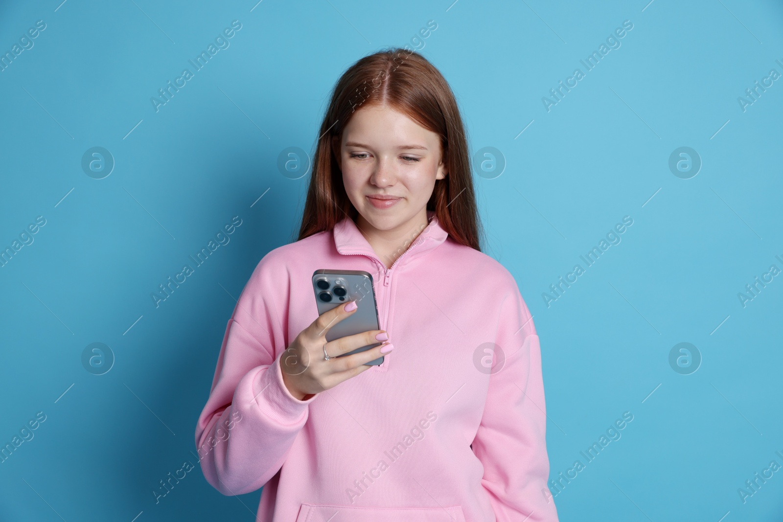 Beautiful teenage girl using smartphone on light blue background Photo of Beautiful teenage girl using smartphone on light blue background