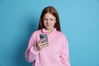 Photo of Beautiful teenage girl using smartphone on light blue background