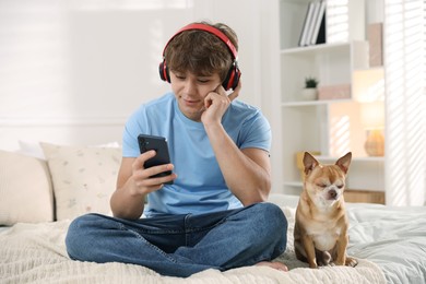 Photo of Teenage boy in headphones using smartphone and dog on bed at home