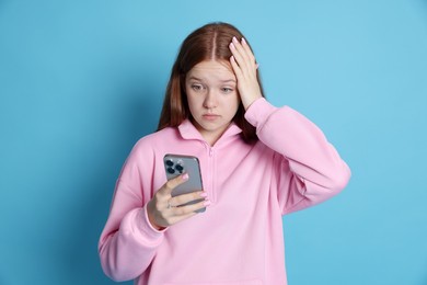 Photo of Emotional teenage girl using smartphone on light blue background