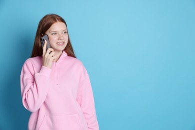 Photo of Smiling teenage girl talking by smartphone on light blue background. Space for text