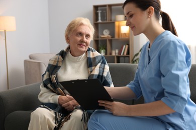 Photo of Nurse with clipboard examining senior woman indoors. Home health care service