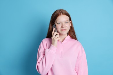 Photo of Beautiful teenage girl talking by smartphone on light blue background