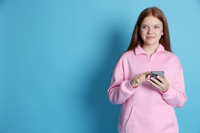 Photo of Beautiful teenage girl with smartphone on light blue background. Space for text
