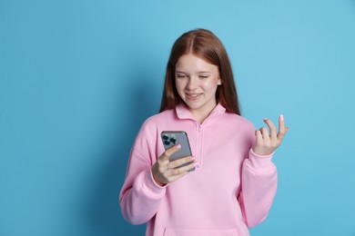 Photo of Smiling teenage girl using smartphone on light blue background