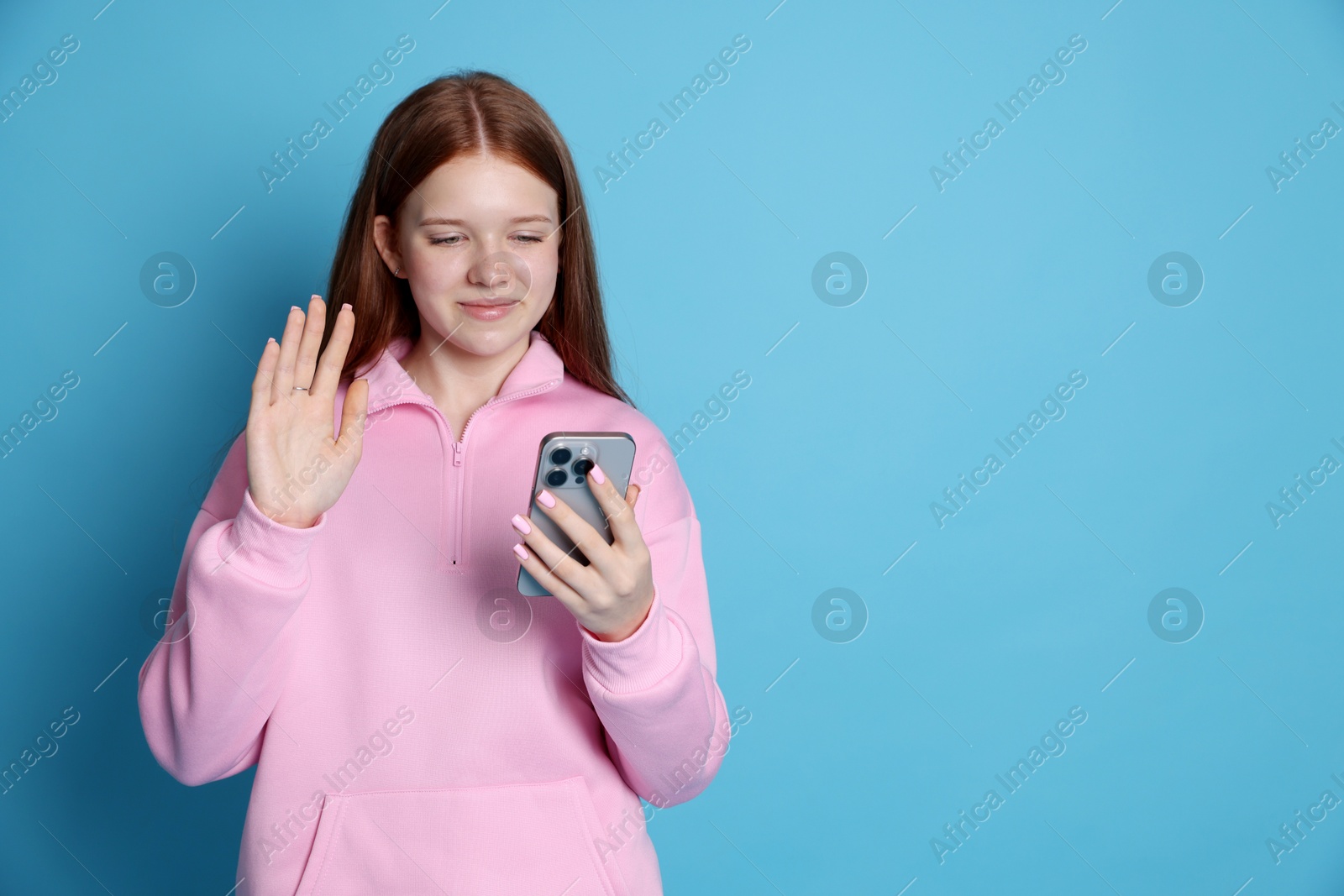 Beautiful teenage girl having videocall by smartphone on light blue background. Space for text Photo of Beautiful teenage girl having videocall by smartphone on light blue background. Space for text
