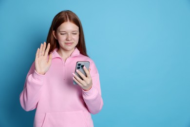 Photo of Beautiful teenage girl having videocall by smartphone on light blue background. Space for text