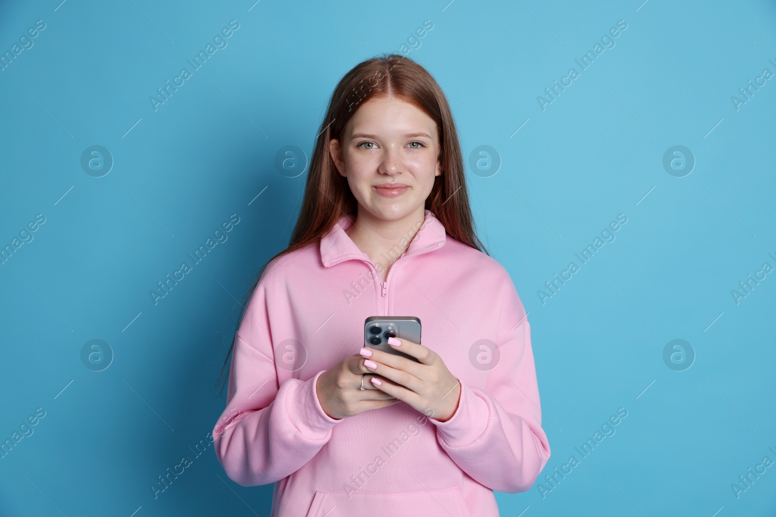 Portrait of beautiful teenage girl with smartphone on light blue background Photo of Portrait of beautiful teenage girl with smartphone on light blue background