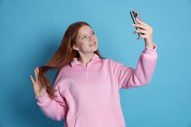 Photo of Smiling teenage girl taking selfie by smartphone on light blue background
