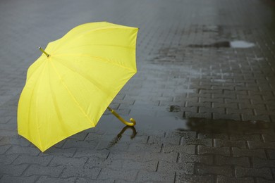 Photo of Yellow umbrella on wet asphalt outdoors, space for text