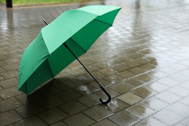 Photo of Green umbrella on wet asphalt under heavy rain, closeup. Space for text