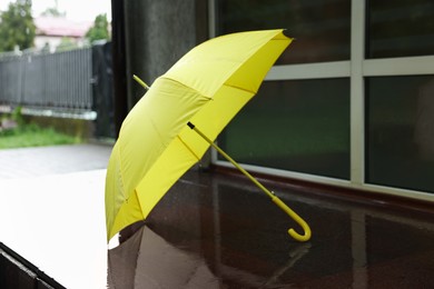 Photo of One yellow umbrella on wet asphalt outdoors