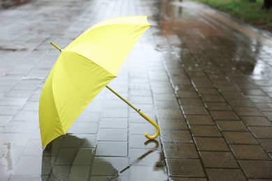 Photo of Yellow umbrella on wet asphalt outdoors, space for text