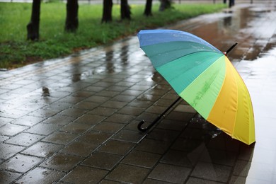 Photo of Colorful umbrella on wet asphalt outdoors, space for text