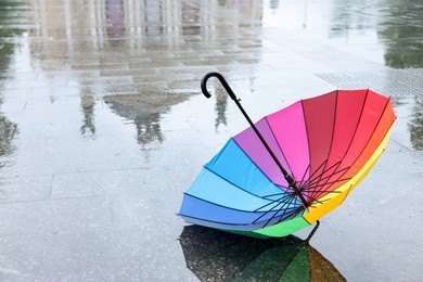 Photo of Colorful umbrella on wet asphalt outdoors, space for text