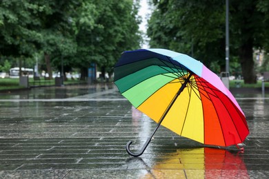 Photo of Colorful umbrella on wet asphalt outdoors, space for text