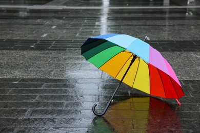 Photo of Colorful umbrella on wet asphalt outdoors, space for text