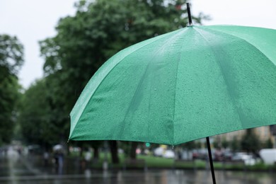 Photo of Green umbrella under heavy rain outdoors, closeup