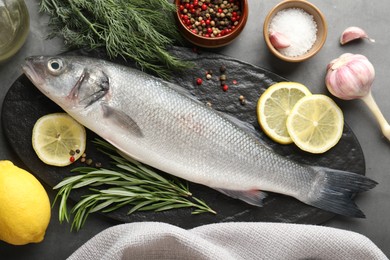 Photo of Fresh raw seabass with spices on grey table, flat lay. Fish and seafood delicacies
