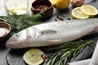 Photo of Fresh raw seabass with spices on grey table, closeup. Fish and seafood delicacies