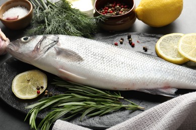 Photo of Fresh raw seabass with spices on grey table, closeup. Fish and seafood delicacies