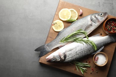 Photo of Fresh raw seabass fish with spices on grey table, top view and space for text. Seafood delicacies