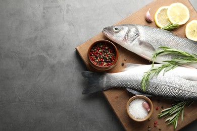 Photo of Fresh raw seabass fish with spices on grey table, top view and space for text. Seafood delicacies