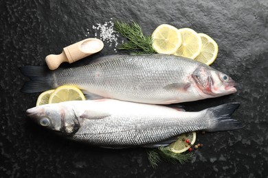 Photo of Fresh raw seabass with spices on black table, flat lay. Fish and seafood delicacies