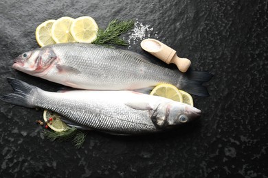 Photo of Fresh raw seabass with spices on black table, flat lay. Fish and seafood delicacies