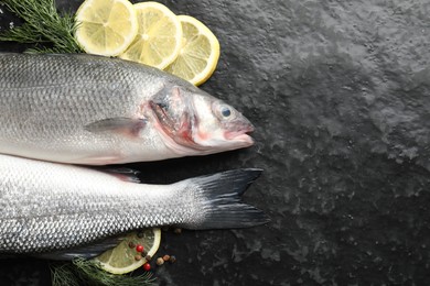 Photo of Fresh raw seabass fish with spices on black table, flat lay and space for text. Seafood delicacies