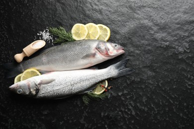 Photo of Fresh raw seabass fish with spices on black table, flat lay and space for text. Seafood delicacies