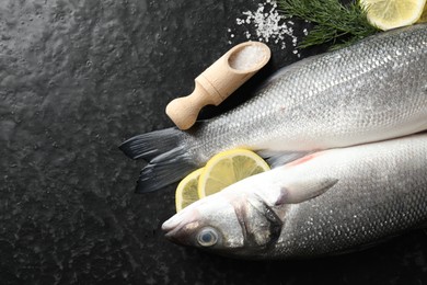 Photo of Fresh raw seabass fish with spices on black table, flat lay and space for text. Seafood delicacies