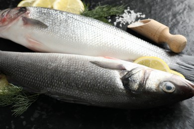 Photo of Fresh raw seabass with spices on black table, closeup. Fish and seafood delicacies