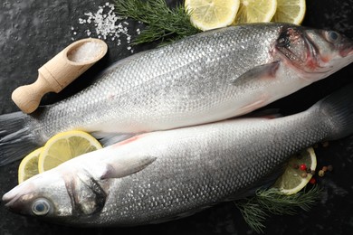 Photo of Fresh raw seabass with spices on black table, flat lay. Fish and seafood delicacies
