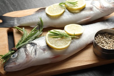 Photo of Fresh raw seabass with spices on black table, closeup. Fish and seafood delicacies