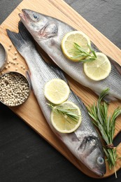 Photo of Fresh raw seabass with spices on black table, top view. Fish and seafood delicacies