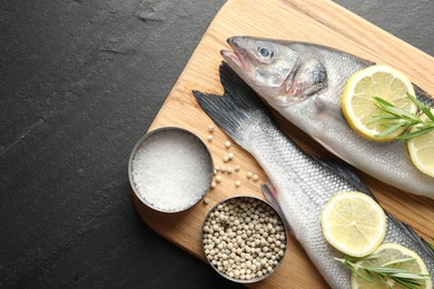 Photo of Fresh raw seabass fish with spices on black table, top view and space for text. Seafood delicacies