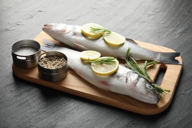 Photo of Fresh raw seabass with spices on black table. Fish and seafood delicacies